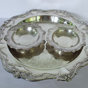 May include: A silver serving tray with two smaller bowls. The tray has a decorative, scalloped edge and the bowls have a similar design.