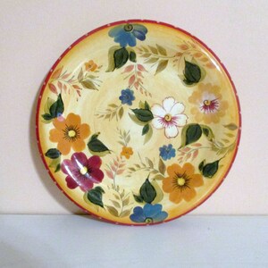 May include: A yellow ceramic plate with a red rim and a white floral design. The flowers are painted in shades of red, orange, yellow, blue, and green.