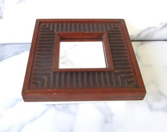 May include: A square wooden mirror with a dark brown frame. The frame has a carved design with vertical lines.