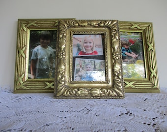 May include: Three gold picture frames with ornate designs. The frames are arranged horizontally with the middle frame slightly larger than the other two. Each frame contains a photo of a child.