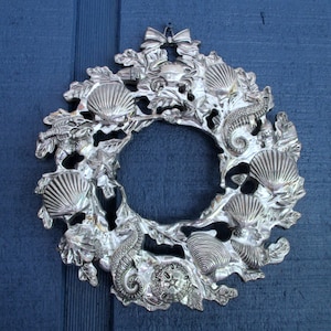May include: Silver-toned metal wreath with a seashell and seahorse design. The wreath is made of a detailed, intricate design.