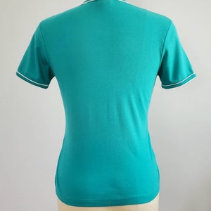 May include: A turquoise short-sleeved t-shirt with a white trim around the neckline and sleeves.