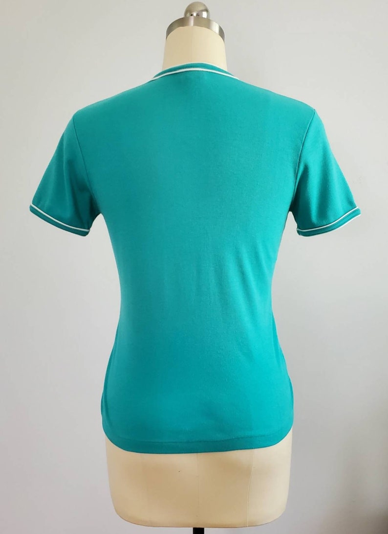 May include: A turquoise short-sleeved t-shirt with a white trim around the neckline and sleeves.