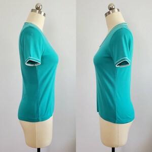 May include: A turquoise short-sleeved shirt with white trim around the neckline and sleeves.