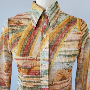 May include: A long-sleeved button-down shirt with a colorful abstract print in shades of orange, yellow, green, and brown. The shirt has a pointed collar and a button-up front.