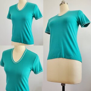 May include: A teal blue short-sleeved t-shirt with a white trim around the neckline and sleeves.