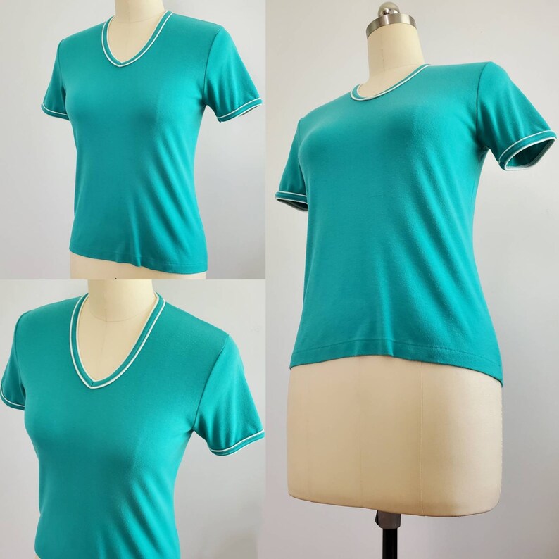 May include: A teal blue short-sleeved t-shirt with a white trim around the neckline and sleeves.
