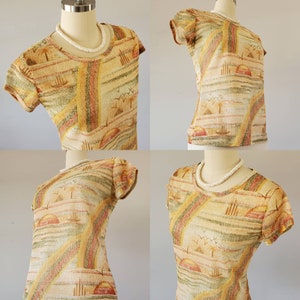 May include: A short-sleeved, multi-colored shirt with a tropical print. The shirt has a light brown, yellow, and green background with a pattern of palm trees, boats, and sunsets.