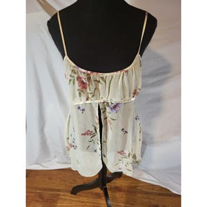 Op de afbeelding: Een crèmekleurige camisole met bloemenprint en spaghettibandjes. De camisole heeft een gerimpelde top en een split aan de voorkant, versierd met rode, paarse en blauwe bloempatronen. Het kledingstuk wordt gepresenteerd op een zwarte mannequin.