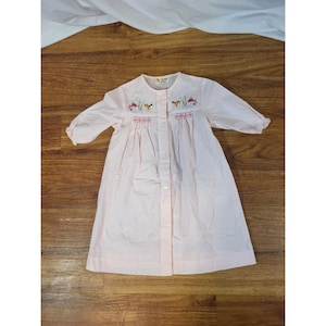 以下が含まれることがあります： 刺繍が施された、ピンク色の長袖ベビーワンピース。 ワンピースはボタン留めフロントと膝丈の裾が特徴です。 刺繍にはカラフルな花と魚が描かれています。 ワンピースは軽量の生地で作られています。