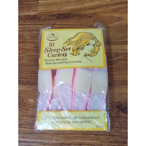 May include: A package of Goody 10 Sleep-Set Curlers. The package is yellow and clear plastic, with text and an illustration of a woman with curly hair. The curlers are white and pink foam. The text reads "No pins. No clips. Now hair setting is so easy."