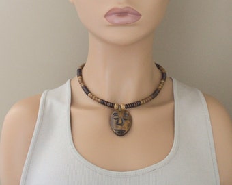 May include: A tan and brown woven fedora hat with a brown leather band and a wooden bead necklace with a carved wooden pendant in the shape of a face.