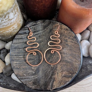 May include: A pair of copper wire earrings with a spiral design. The earrings are displayed on a wooden surface.
