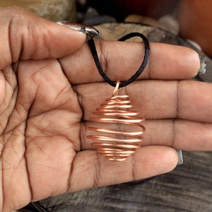 May include: A copper wire cage pendant on a black cord. The cage is oval shaped and has a spiral design.