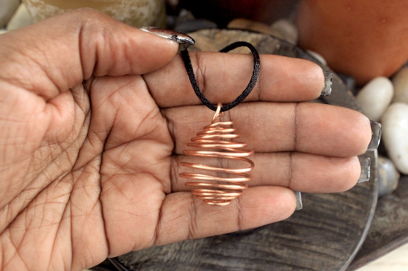May include: A copper wire cage pendant on a black cord. The cage is oval shaped and has a spiral design.