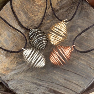 May include: Four wire-wrapped pendants in different colors, including silver, gold, and copper, are displayed on a wooden surface. Each pendant is a spiral shape and hangs from a black cord.