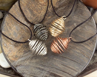 May include: Four wire-wrapped pendants in different colors, including silver, gold, and copper, are displayed on a wooden surface. Each pendant is a spiral shape and hangs from a black cord.