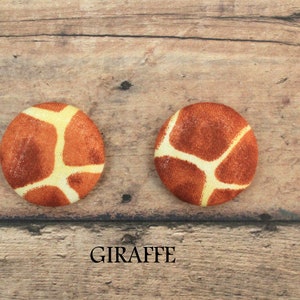 Pu&ograve; includere: Due bottoni rotondi con stampa di giraffa. I bottoni sono marroni con macchie gialle e sono su uno sfondo di legno. Il testo "GIRAFFE" &egrave; stampato sotto i bottoni.