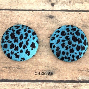 Pu&ograve; includere: Due bottoni rotondi in tessuto con un motivo a stampa leopardata. I bottoni sono blu con macchie nere. Il testo "CHEETAH" &egrave; stampato sotto i bottoni.