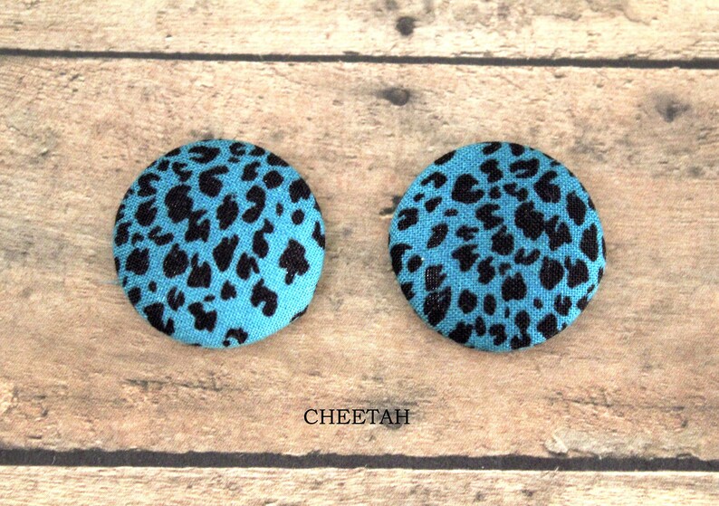 Pu&ograve; includere: Due bottoni rotondi in tessuto con un motivo a stampa leopardata. I bottoni sono blu con macchie nere. Il testo "CHEETAH" &egrave; stampato sotto i bottoni.