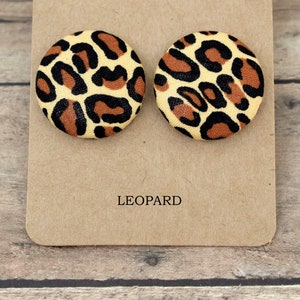 Pu&ograve; includere: Un paio di orecchini rotondi con stampa leopardata su una carta marrone con la scritta "LEOPARD" stampata su di essa.