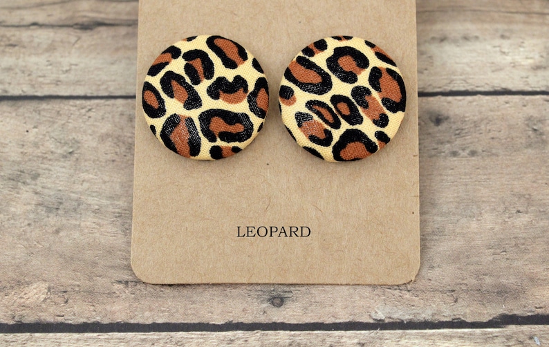 Pu&ograve; includere: Un paio di orecchini rotondi con stampa leopardata su una carta marrone con la scritta "LEOPARD" stampata su di essa.