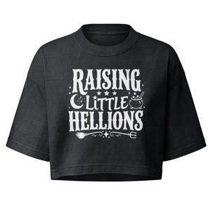May include: A black cropped t-shirt featuring white screen-printed text that reads "RAISING LITTLE HELLIONS" with graphic icons including a crescent moon, stars, a bubbling cauldron, a broomstick, and a pitchfork centered on the front chest.