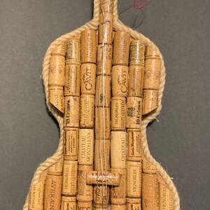Pu&ograve; includere: Un violino realizzato interamente con tappi di sughero per vino, con un bordo in corda marrone e un'etichetta nera che dice "Black Swan".