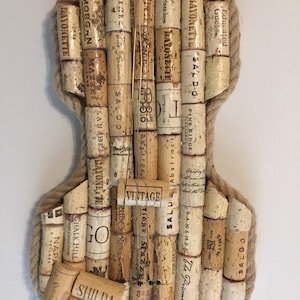 Pu&ograve; includere: Un'opera d'arte da parete a forma di violino realizzata con tappi di vino. I tappi sono disposti in uno schema che ricorda il corpo di un violino. I tappi sono tenuti insieme da uno spago. I tappi hanno varie etichette, tra cui "Bayonette", "The Prisoner", "Saldo", "Morgan", "Mazzei" e "Chalk Hill".
