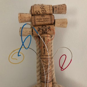 Pu&ograve; includere: Un violino fatto a mano con tappi di vino, con un manico di corda e corde di filo metallico colorato. I tappi sono etichettati con i nomi di diversi vini, tra cui "Clos du Bois" e "Santa Rita 1201".