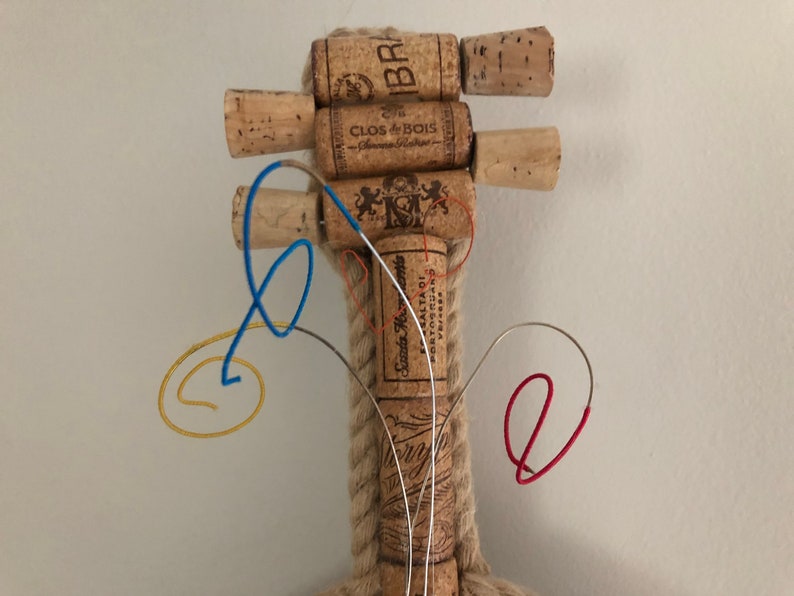 Pu&ograve; includere: Un violino fatto a mano con tappi di vino, con un manico di corda e corde di filo metallico colorato. I tappi sono etichettati con i nomi di diversi vini, tra cui "Clos du Bois" e "Santa Rita 1201".