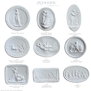 May include: A collection of white plaster intaglios, each featuring classical relief sculptures. The designs include Venus de Milo, Cupid and Psyche, and scenes of mythological figures. The intaglios are large, measuring 2 to 3 inches.