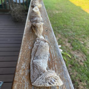 May include: A long, translucent, and shed snake skin with a distinct, repeating diamond-shaped scale pattern. The skin is pale, off-white, and grayish in color, appearing dry and delicate as it lies stretched out in a linear, slightly crumpled formation.