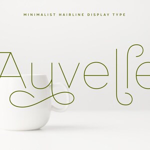 May include: A white ceramic mug with the word "Auvelle" in a minimalist green font. The text "MINIMALIST HAIRLINE DISPLAY TYPE" is above the word. The mug is on a white surface.
