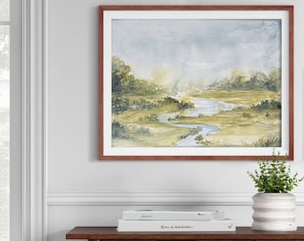 May include: Watercolor landscape art print in a brown frame. The artwork depicts a winding river through a green and yellow field, with trees and a light blue sky. The print is displayed above a wooden table with books and a white and gray striped vase.
