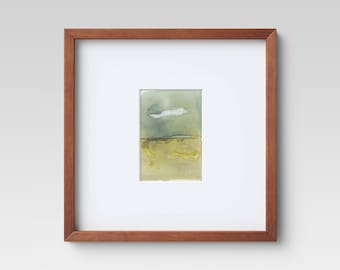 May include: A framed watercolor painting of a landscape with a single white cloud in a blue sky over a yellow field.