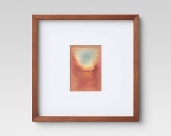 May include: A framed abstract watercolor painting with a brown wooden frame. The painting features a soft, blended background of orange, red, and yellow with a blue-green cloud-like shape in the center.