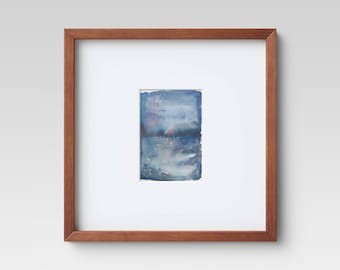 May include: A framed watercolor painting with a brown wooden frame. The artwork features a rectangular abstract design in shades of blue, with hints of pink and white, creating a serene, atmospheric effect. The painting is mounted on a white mat.