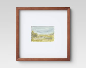 May include: A framed watercolor painting of a landscape with a small stream, green trees, and a cloudy sky. A small bird flies in the sky.