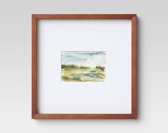 May include: A framed watercolor landscape painting. The artwork features a serene scene with a blue sky, yellow and green fields, and a body of water. The painting is set within a white mat and a brown wooden frame.
