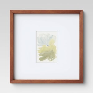 May include: A framed watercolor painting with a light brown wooden frame. The artwork features abstract brushstrokes in shades of pale blue, yellow, and olive green on a white background. The frame is square and has a simple, clean design.