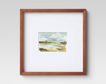 May include: A framed watercolor painting of a landscape with a river, green trees, and a cloudy sky.