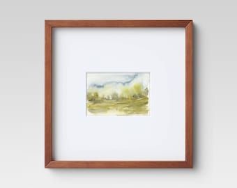 May include: A framed watercolor painting of a landscape with green trees and a blue sky. The painting is in a simple brown frame.