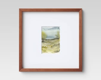 May include: Watercolor landscape art print in a brown wooden frame. The artwork features a serene scene with muted greens, blues, and yellows, depicting a field and sky. The frame is a warm, natural wood tone.