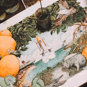 May include: A watercolour painting depicting a variety of Florida wildlife and plants. The painting features a space shuttle launching into the sky, a manatee swimming in the water, an alligator, a pink roseate spoonbill, and a variety of plants, including orange trees, palm trees, and cacti.