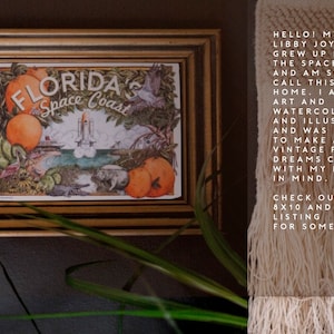 May include: A framed vintage postcard print of Florida's Space Coast featuring a rocket ship, oranges, and palm trees. The text "FLORIDA'S Space Coast" is printed on the postcard.