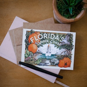 May include: A postcard featuring a colourful illustration of a space shuttle launching over a beach with palm trees and oranges. The text on the postcard reads "Florida's Space Coast".