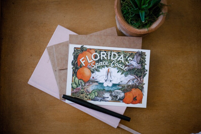 May include: A postcard featuring a colourful illustration of a space shuttle launching over a beach with palm trees and oranges. The text on the postcard reads "Florida's Space Coast".