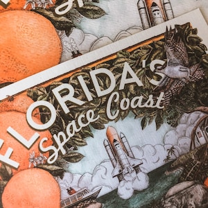 May include: A vintage-style illustration of a space shuttle launching from the Florida Space Coast. The image features a vibrant green, blue, and orange colour palette with a white background. The text "FLORIDA'S Space Coast" is prominently displayed in a white, serif font.