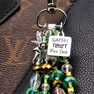 May include: A green and gold beaded keychain with a silver charm that says "Faith Trust Pixie Dust".